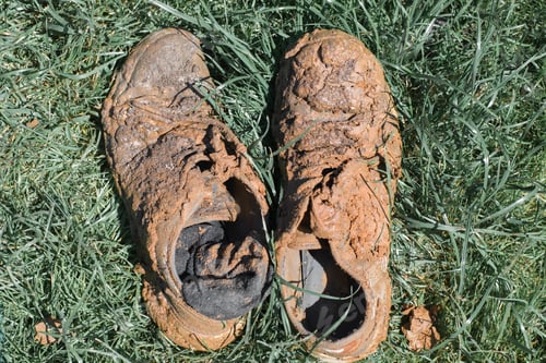 Preview: Dirty boots and socks in mud and clay on green grass outdoors. Close-up, top view, no people
