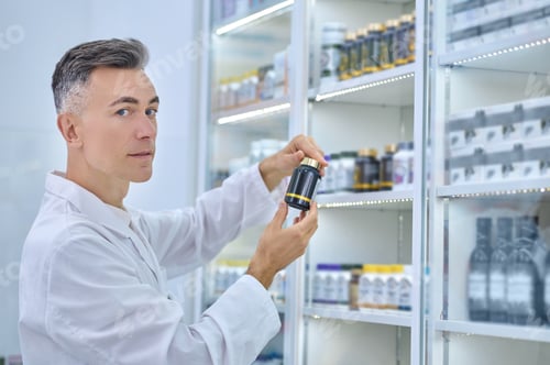 Preview: Male druggist holding a dietary supplement in his hands