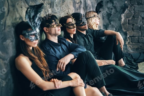 Preview: Group of friends in masquerade carnival mask sitting on floor relax after party