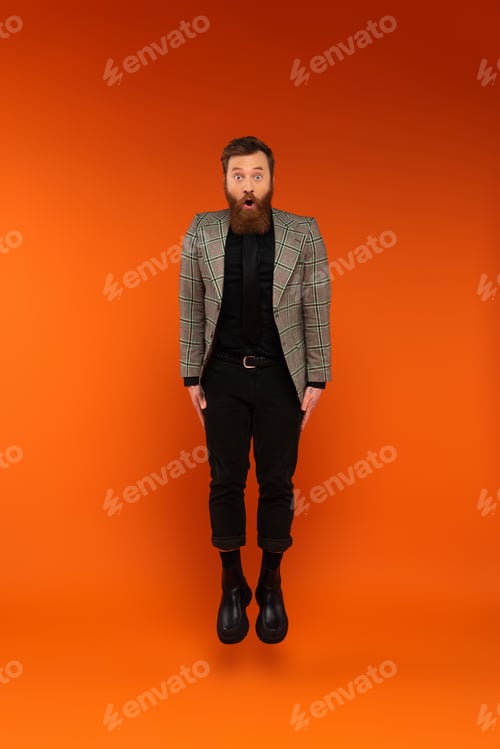 Preview: Shocked man in stylish outfit jumping on red background