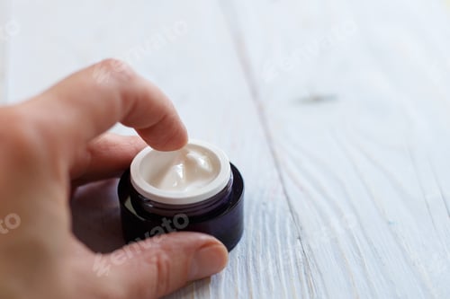 Preview: Hands of a girl with a jar of face cream close up applied to the finger of woman's hand