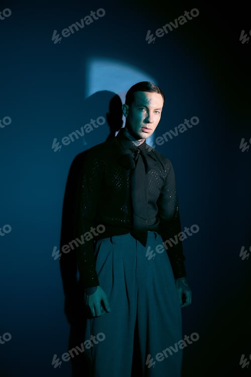 Preview: Handsome young man showcases stylish fashion against a striking blue backdrop in soft light