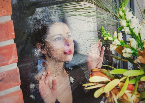 Preview: woman at the wet window after the rain misses the plants standing outside the window.