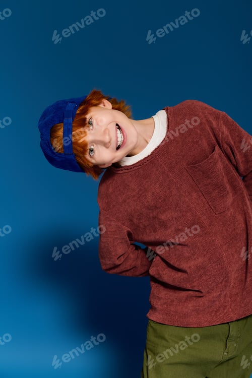 Preview: Bright and cheerful redhead boy showcasing casual fashion in a modern studio setting