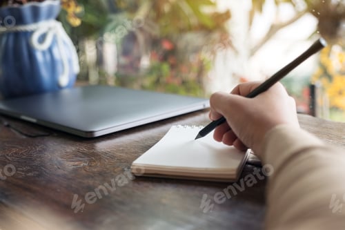 Preview: Closeup image of hand writing down on a blank notebook on wooden table