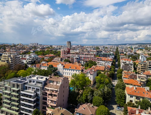 Preview: Aerial view of a vibrant cityscape with residential buildings and green trees under a blue sky
