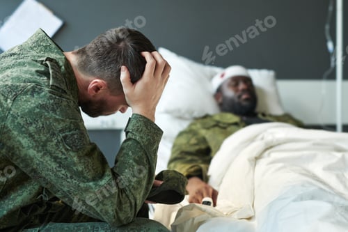 Preview: Young worried soldier in camouflage touching head while sitting by his friend