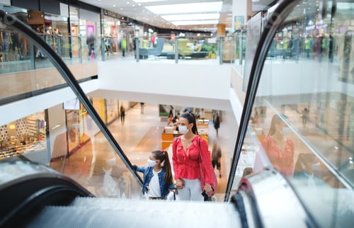 Preview: Mother and daughter with face mask on escalator indoors in shopping center, coronavirus concept