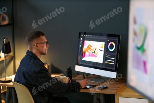 Preview: Young Adult Caucasian Man Editing Photo on Computer in Modern Workspace