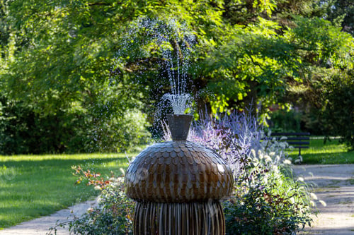 Preview: Water fountain surrounded by green plants and flowers in a sunny park