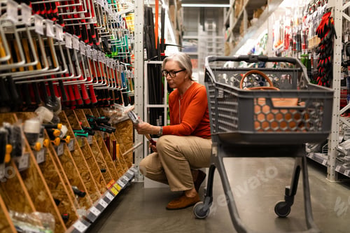 Preview: Older woman shopping for tools in a well-organized home improvement store aisle during the day