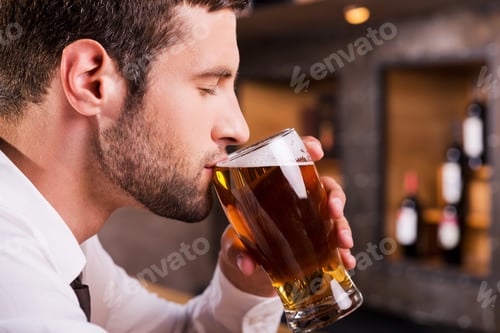 Preview: Man drinking beer. Side view of handsome young man drinking beer while sitting at the bar counter