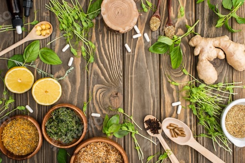 Preview: top view of pills and green herbs on wooden surface, naturopathy concept