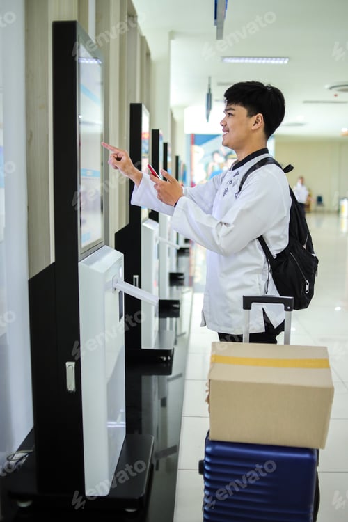 Preview: Asian Man Holding Mobile Phone While Using Self Service Check-in Machine at Airport.