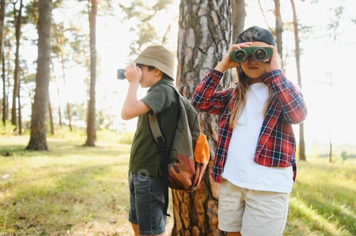 Preview: boy and girl go hiking with backpacks on forest road bright sunny day