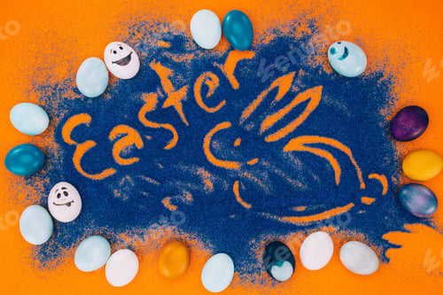 Preview: top view of easter sign with rabbit made of blue sand with chicken eggs on orange