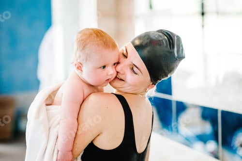 Preview: Happy young mother swimming instructor holding a baby in her arms in the towel. After swimming,