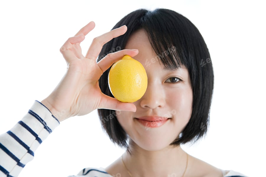 Cover for Smiling woman playfully holding a lemon over her eye