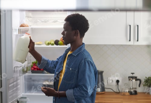 Preview: Black man taking milk from refrigerator cooking dinner at home