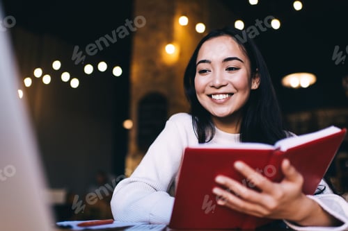 Preview: Happy young woman with book in cafe