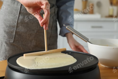 Preview: Woman cooking delicious crepe on electrical pancake maker in kitchen, closeup
