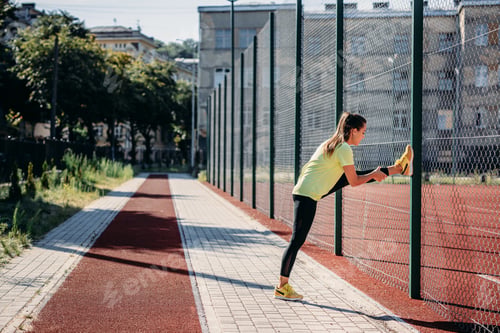 Preview: Flexible woman stretching legs near chain link fence