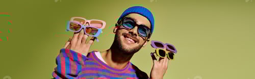 Preview: Handsome young man showcases vibrant fashion in trendy sunglasses against green backdrop