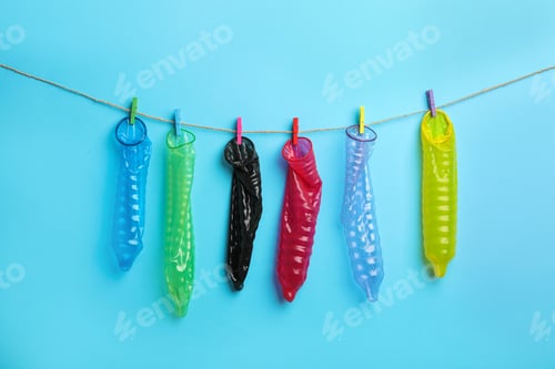 Preview: Used colorful condoms hanging on clothesline against light blue background. Safe sex concept