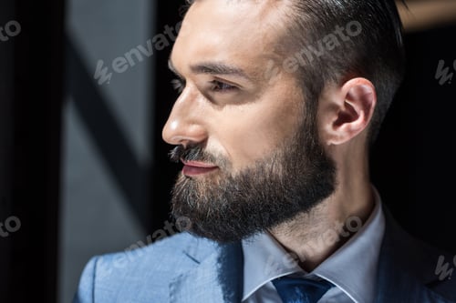 Preview: portrait of handsome bearded businessman in grey suit looking away
