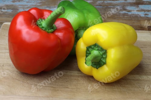 Preview: Fresh red, green, and yellow bell peppers on a wooden cutting board