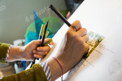 Preview: Close up of woman sitting at a drawing board, drawing with a fineliner, using a design template.