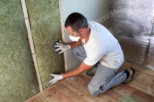 Preview: Worker in protective goggles and respirator insulating rock wool insulation in wooden frame