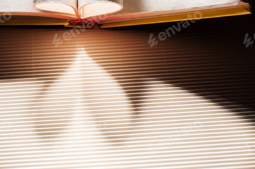 Preview: Open book with folded pages on textured surface with heart-shaped shadow