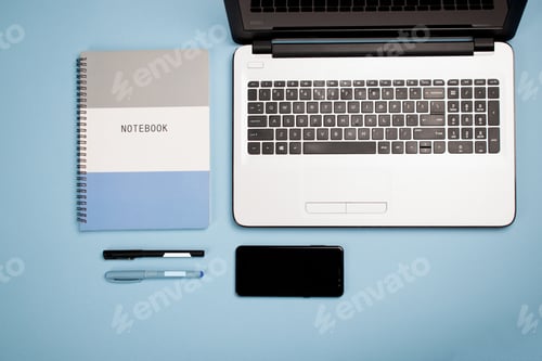 Preview: Top view of a laptop, notepad, pens, and a smartphone on a blue backgroun
