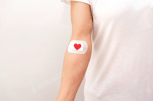 Preview: close up of blood donor arm with bandage and red heart on grey background, blood donation concept