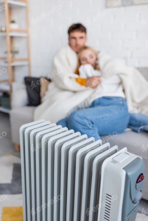 Preview: modern radiator heater near blurred couple hugging and sitting on couch under blanket