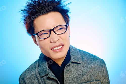 Preview: Stylish young man with spiky hair and glasses expresses playful emotion in bright blue backdrop