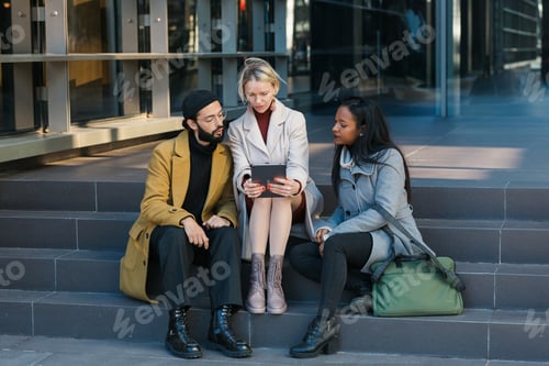 Preview: Diverse colleagues using tablet on street while sitting on steps