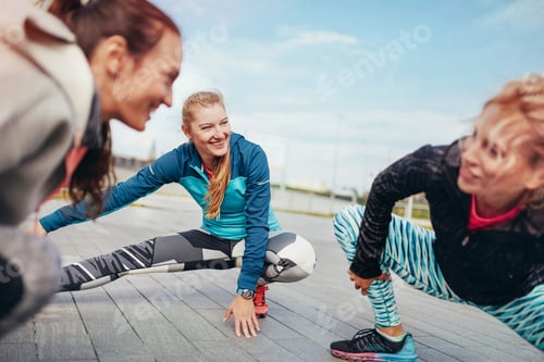 Preview: Three female runners crouching and stretching on pier