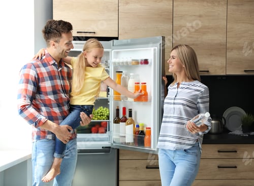 Preview: Happy family with bottle of water near refrigerator in kitchen