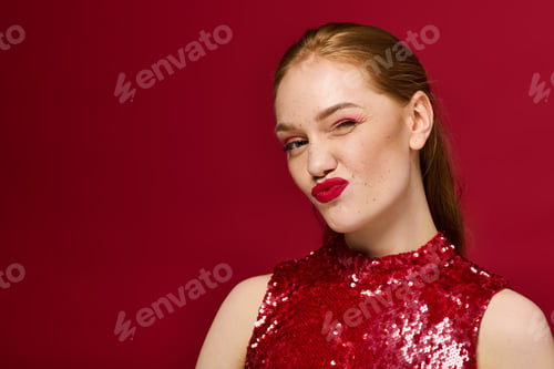 Preview: Young beautiful woman posing with confidence against a vibrant red background in a stylish outfit