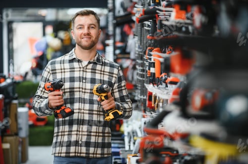 Preview: Portrait of young bearded man buying modern electric drill while standing in tool