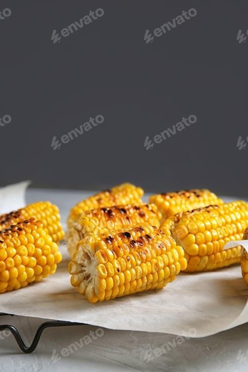 Preview: Cooling rack with grilled corn cobs on table against gray background. Space for text