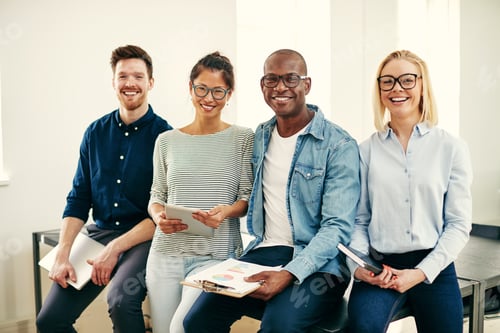 Preview: Smiling group of young businesspeople sitting on an office table