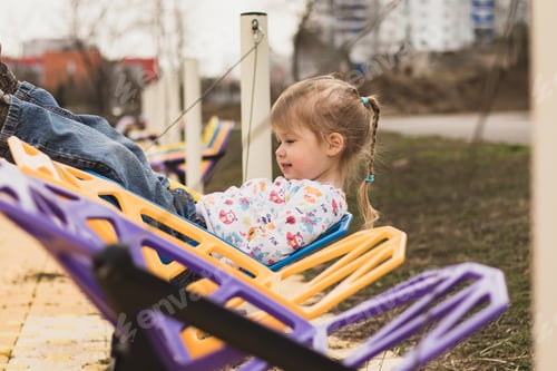 Preview: A little funny girl having fun riding on a colorful swing in a city park