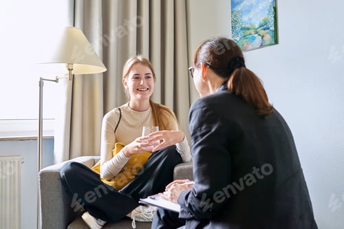 Preview: Young female teenager talking with counselor, teacher sitting in chair in office