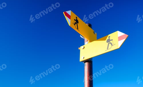 Preview: Directional marker for a mountain hike. Yellow bright sign with an arrow against the blue sky.