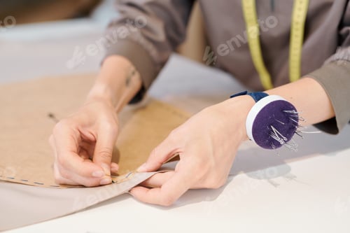 Preview: Hands of young seamstress pinning cut sketch to textile