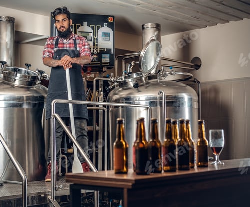 Preview: Indianr male manufacturer presenting craft beer in the microbrewery.