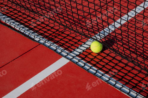 Preview: Tennis ball next to the net of a red hard surface tennis court